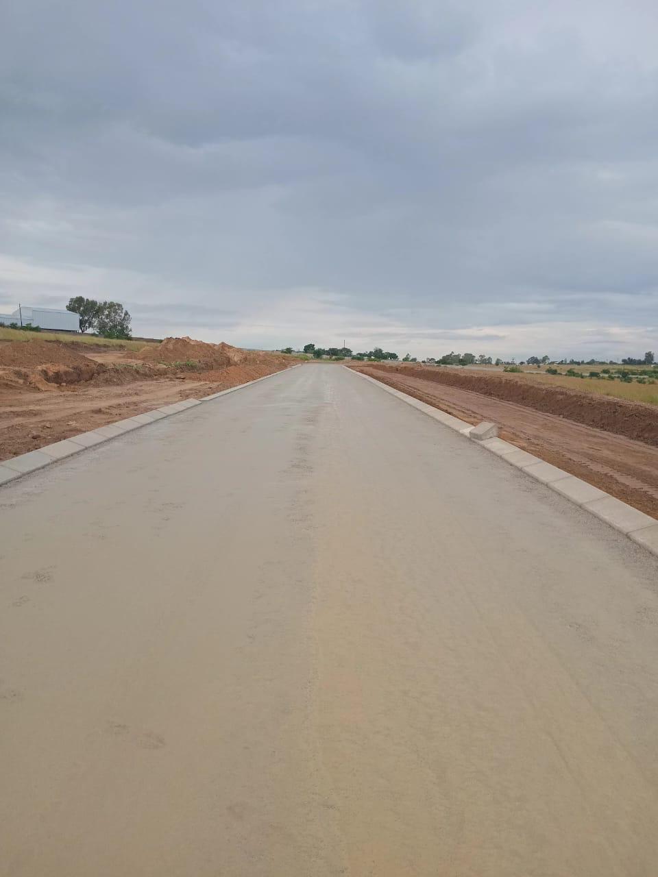 Freshly laid asphalt surface stretching along a newly constructed road with red soil shoulders on either side